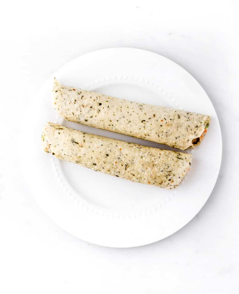 Two veggie tortilla roll ups ready to be sliced into pinwheels.