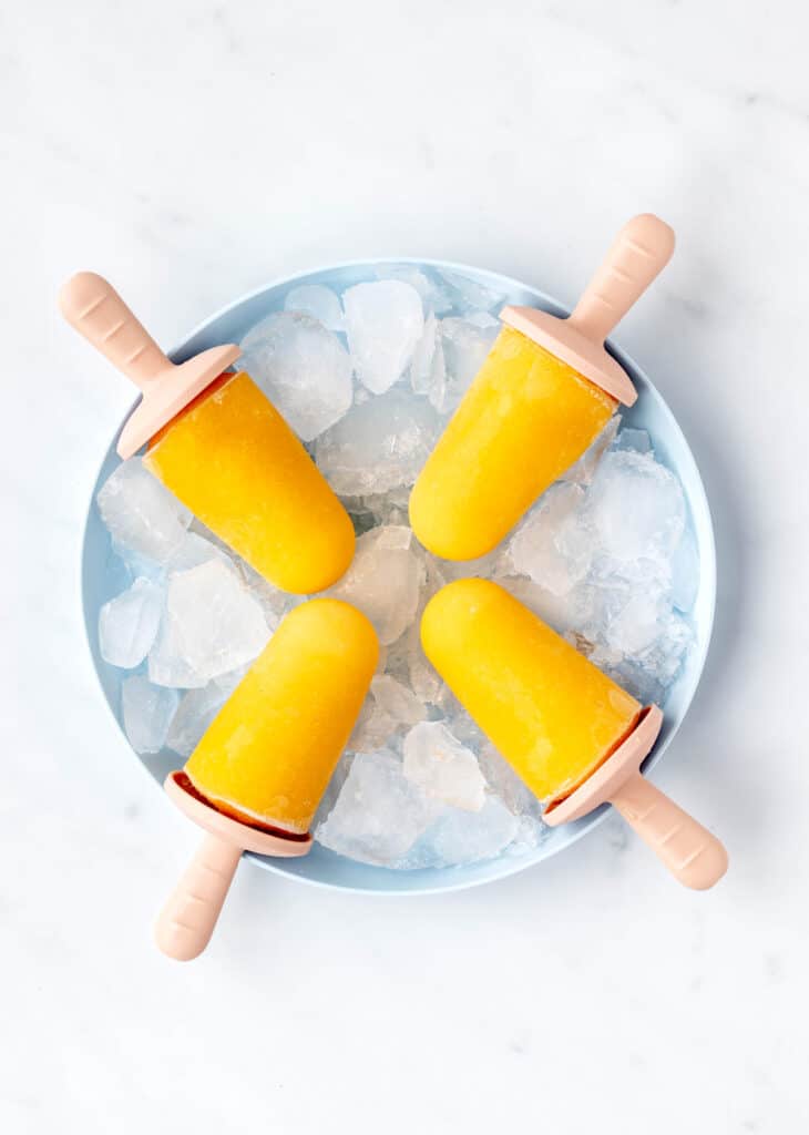 Four mango popsicles on a blue plate with ice.
