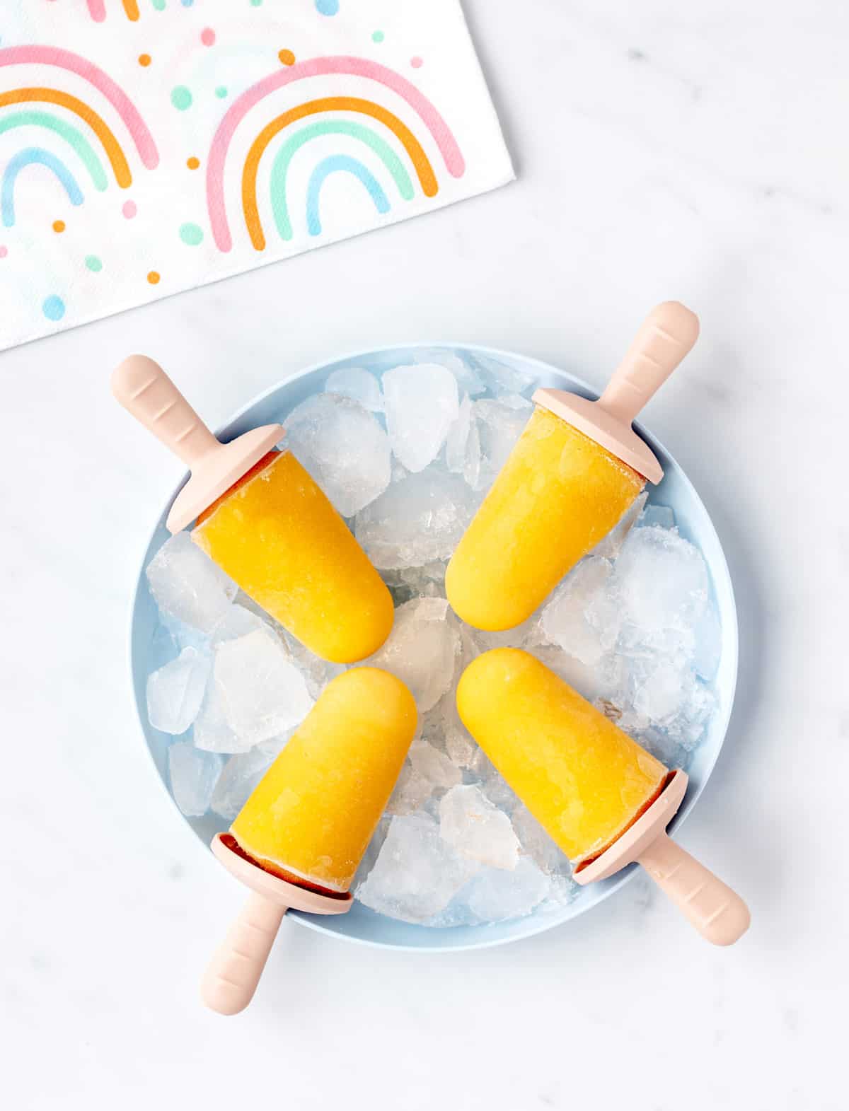 Four mango popsicles for toddlers on a plate of ice.