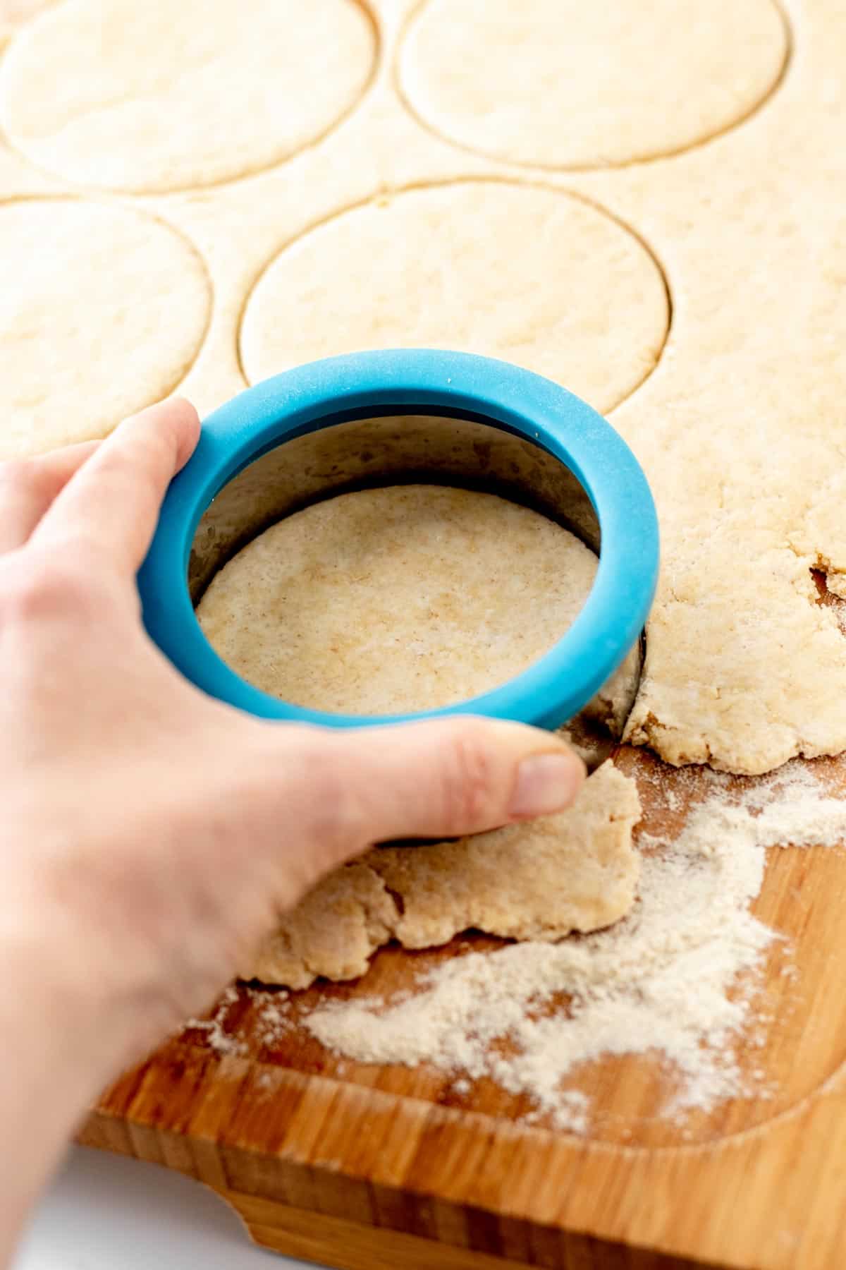 A hand pressing a circular cookie cutter into homemade pizza dough to make mini pizzas.