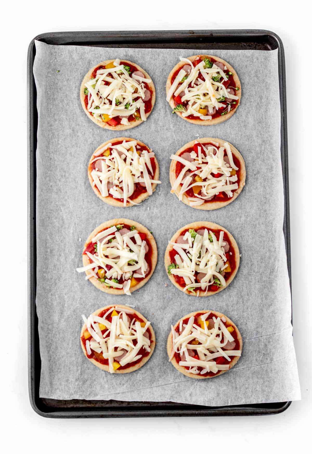 Toppings on the homemade mini pizzas on a baking sheet ready to be cooked.