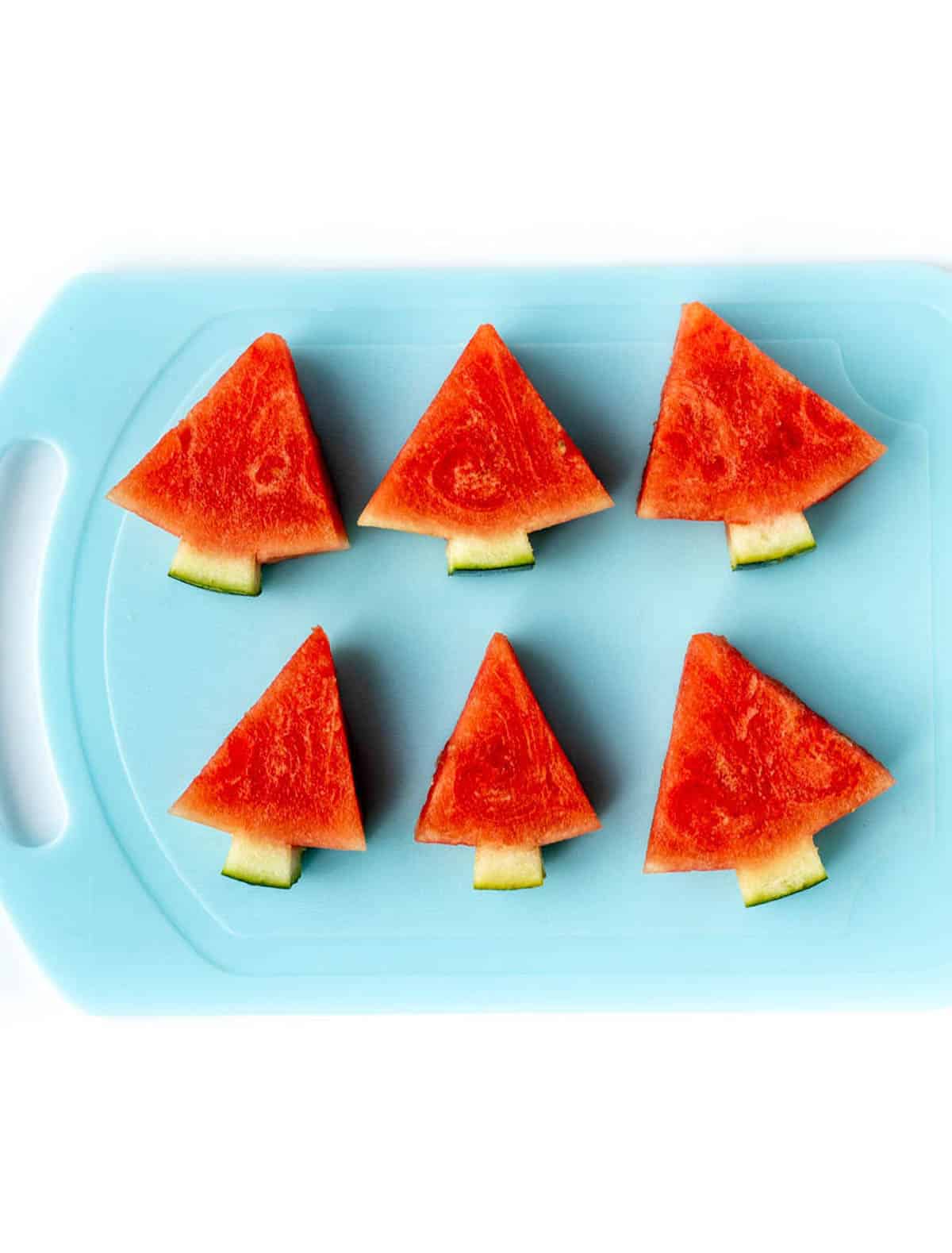 Six watermelon Christmas trees on a blue cutting board.