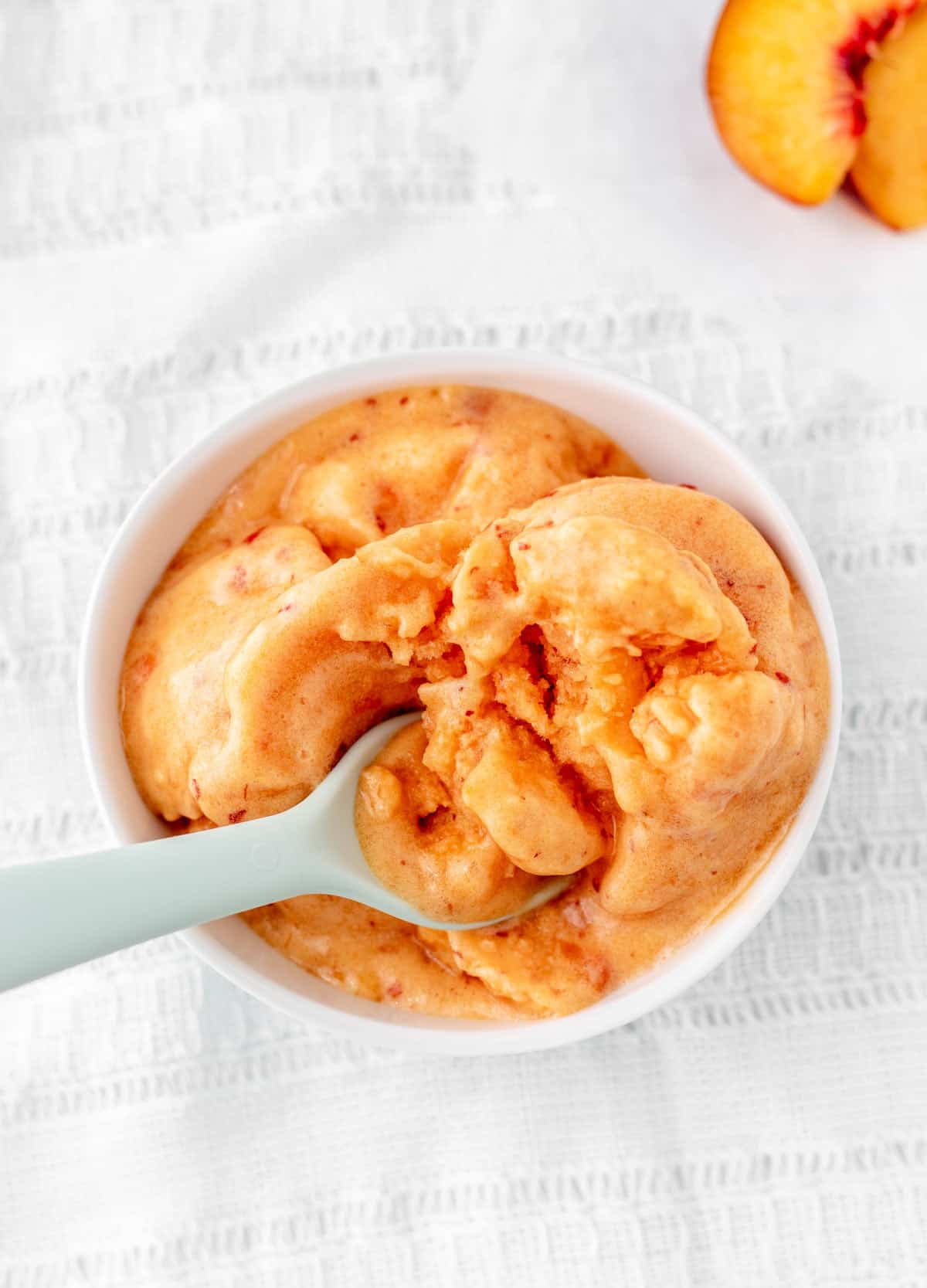 An overhead image of a spoon digging into a bowl of 3 ingredient peach sorbet.