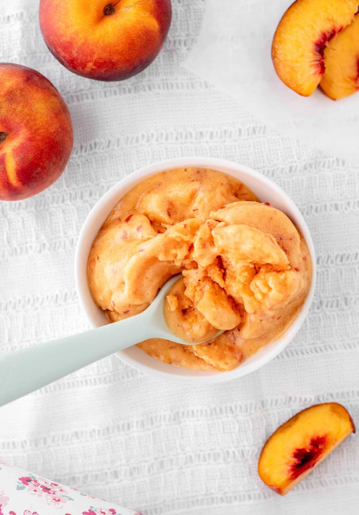 An overhead image of a spoon digging into a bowl of 3 ingredient peach sorbet.
