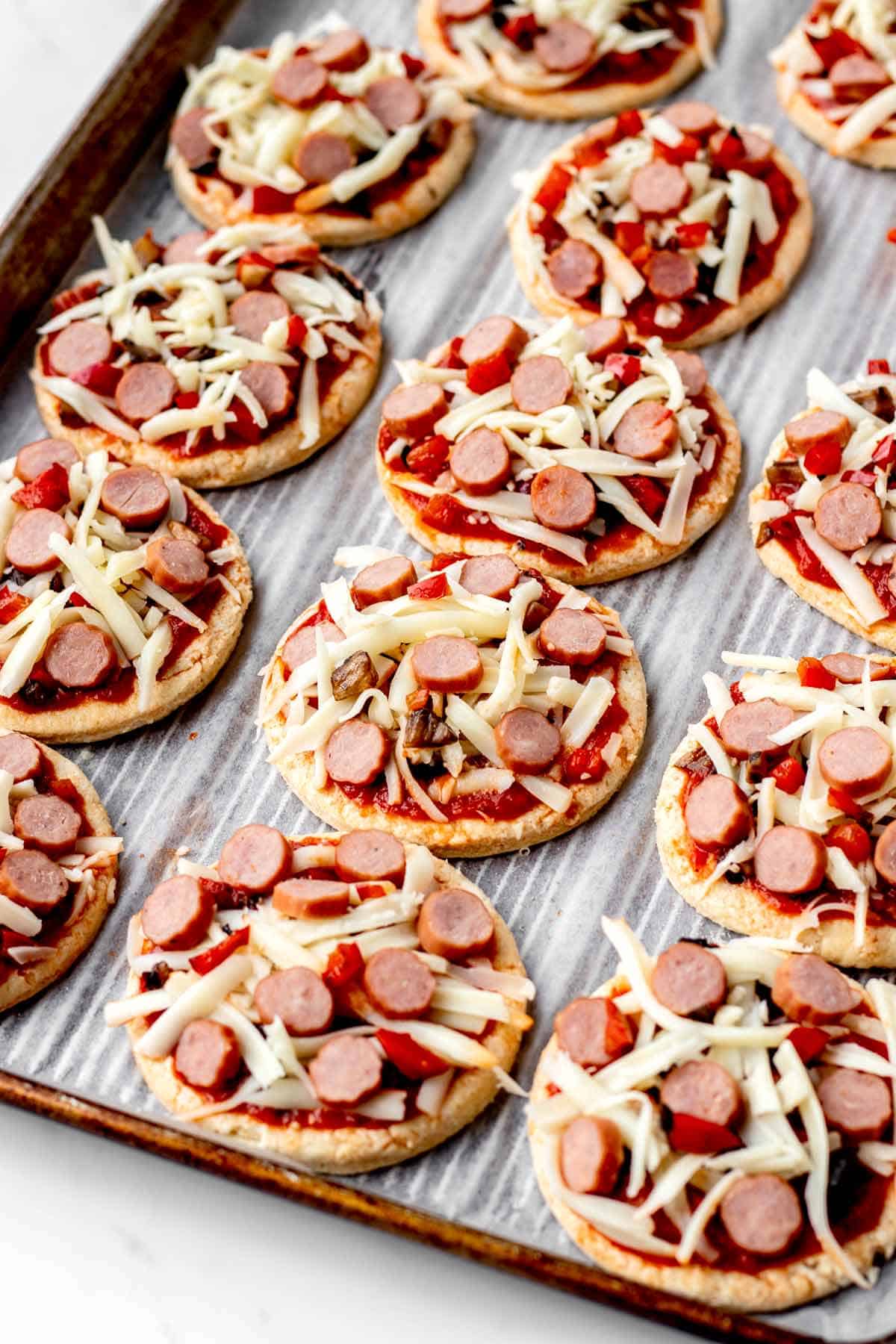 Mini pizzas loaded with toppings on a baking sheet.