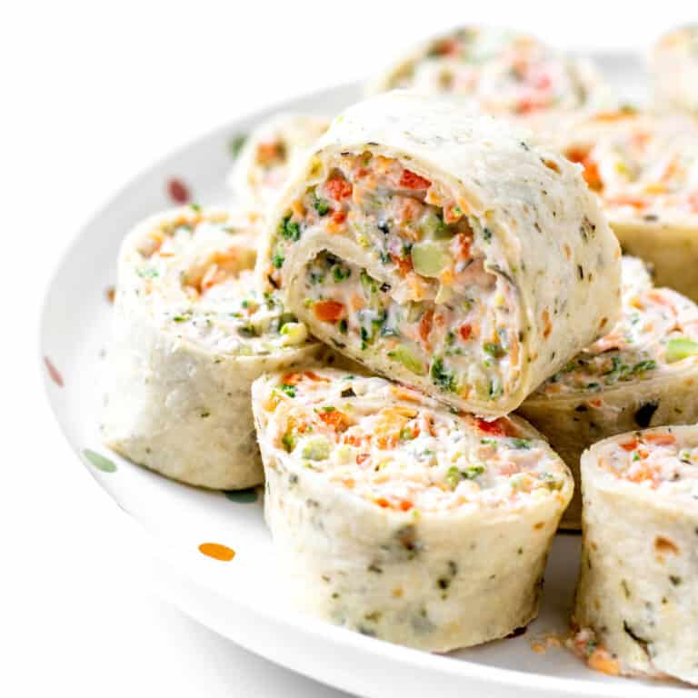 A veggie pinwheel with cream cheese stacked on top of other roll ups on a plate.