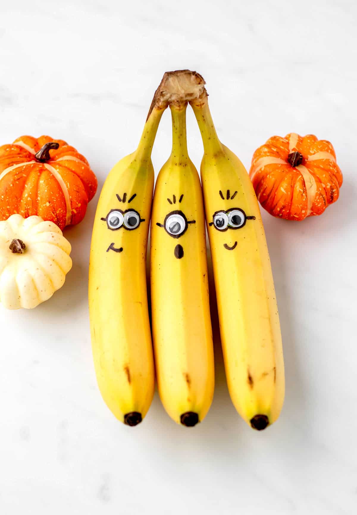 Three minion bananas next to pumpkins.