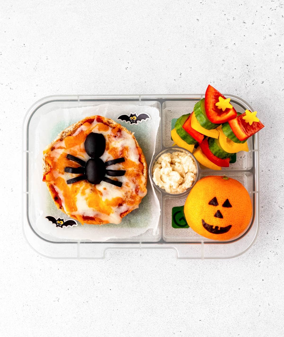 Halloween lunch box with spider pizza, veggie skewers and a jack o lantern clementine.