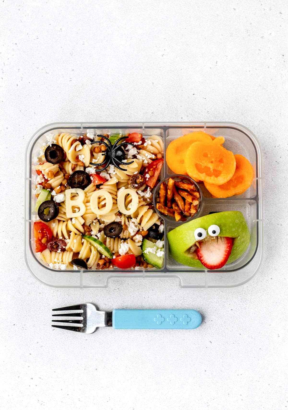 Halloween lunch box with halloween pasta salad with "boo" written on it, pumpkin cantaloupe, pretzels and apple monster.