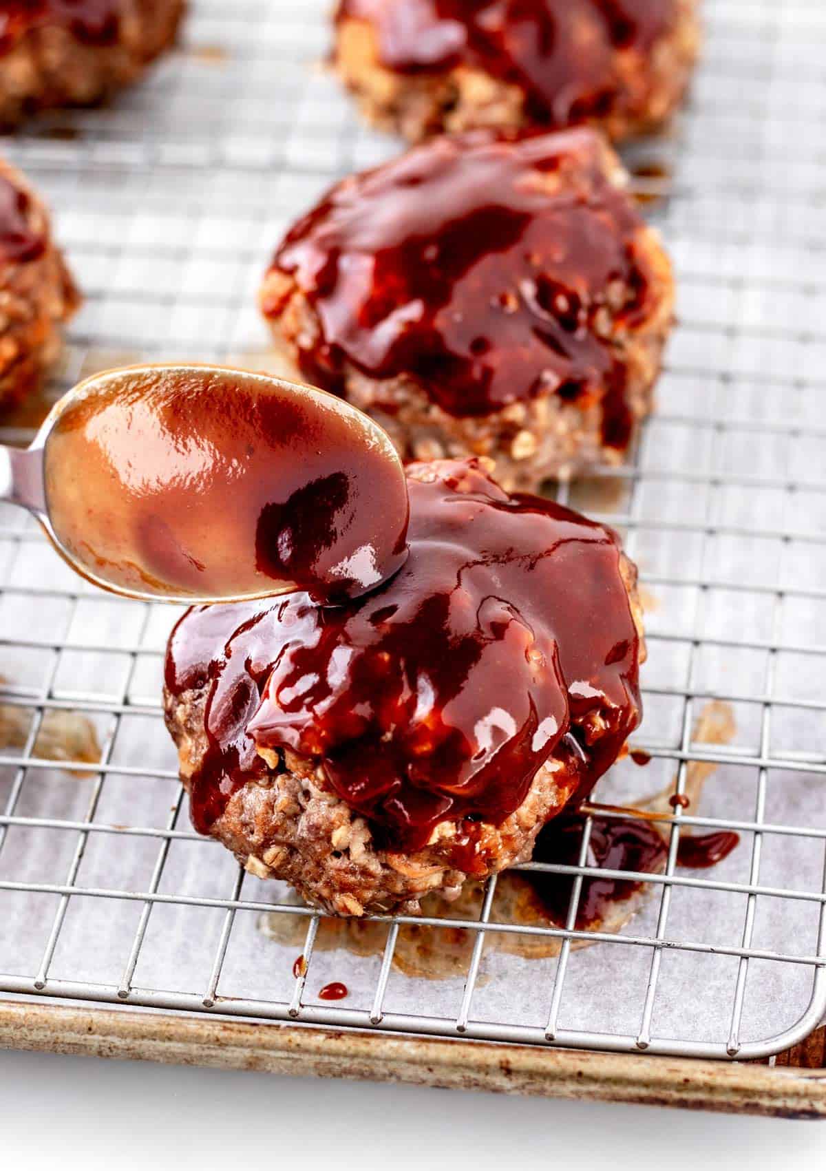 A spoon topping each mini meatloaf with homemade glaze.