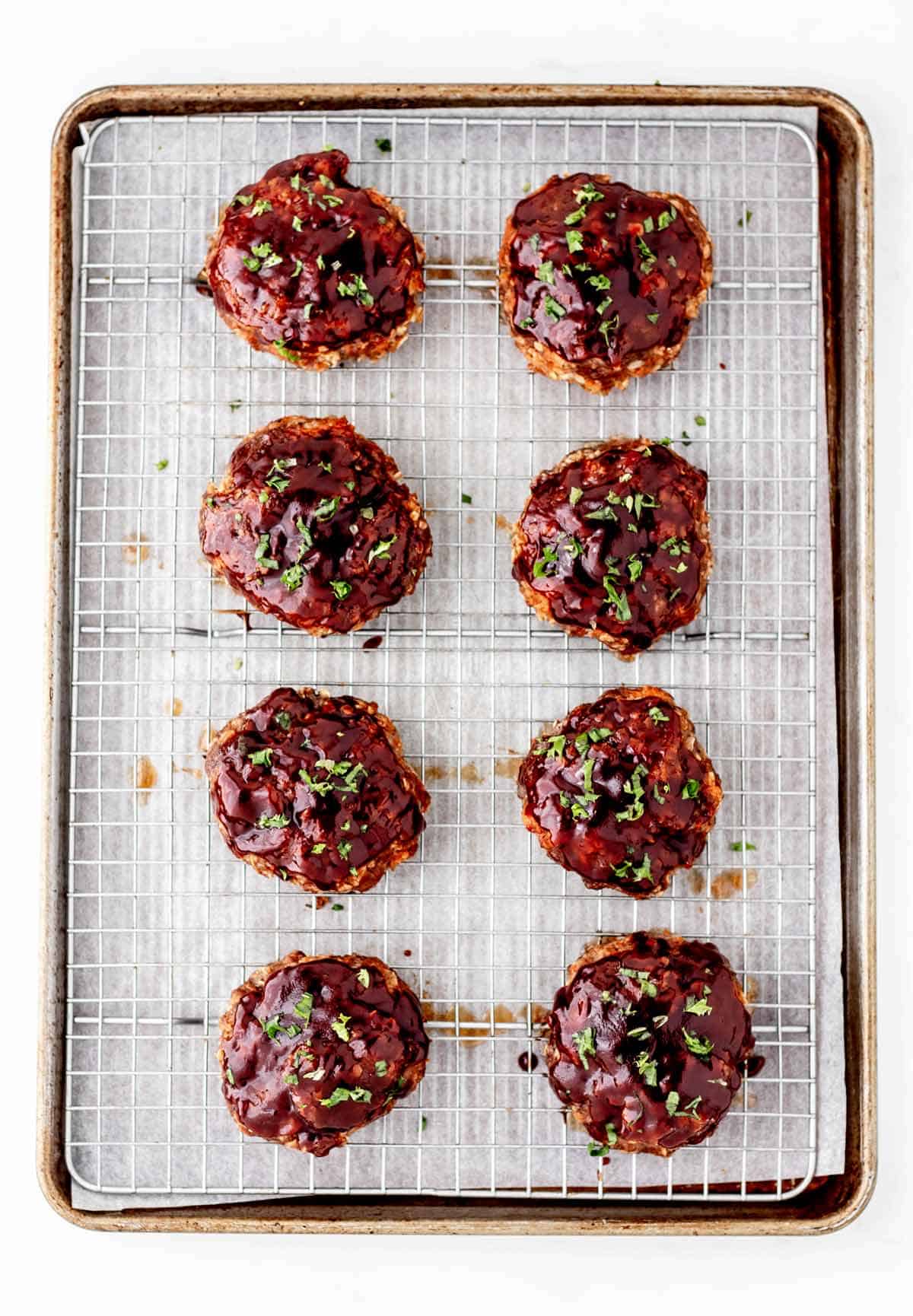Overhead image of eight baked mini meatloaves on a baking sheet topped with parsley.