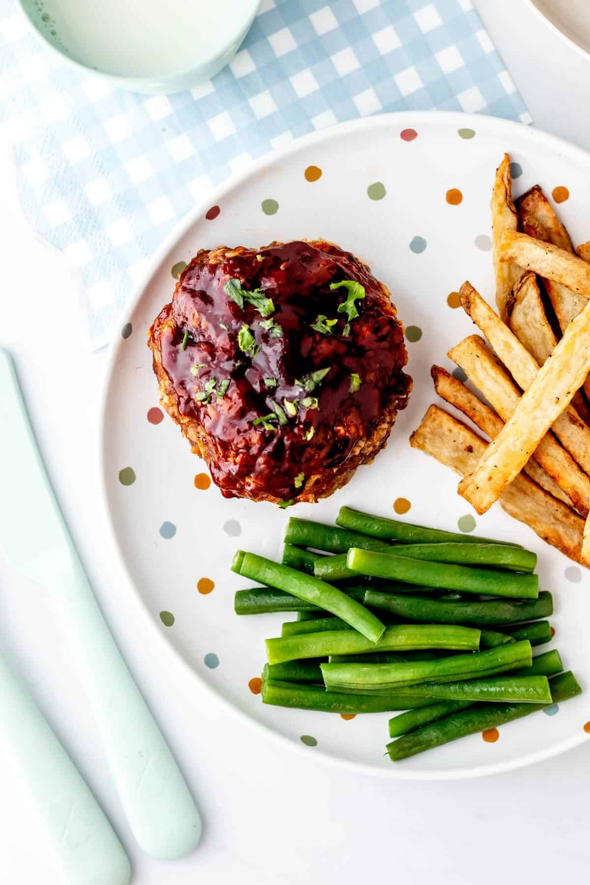 An overhead image of a healthy mini meatloaf on a plate with homemade french fries and green beans.