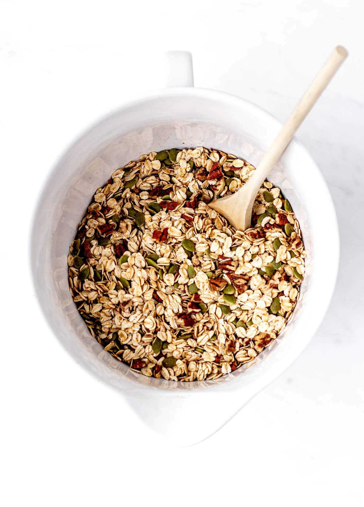 Oats, pumpkin seeds and pecans combined in a bowl to make granola.