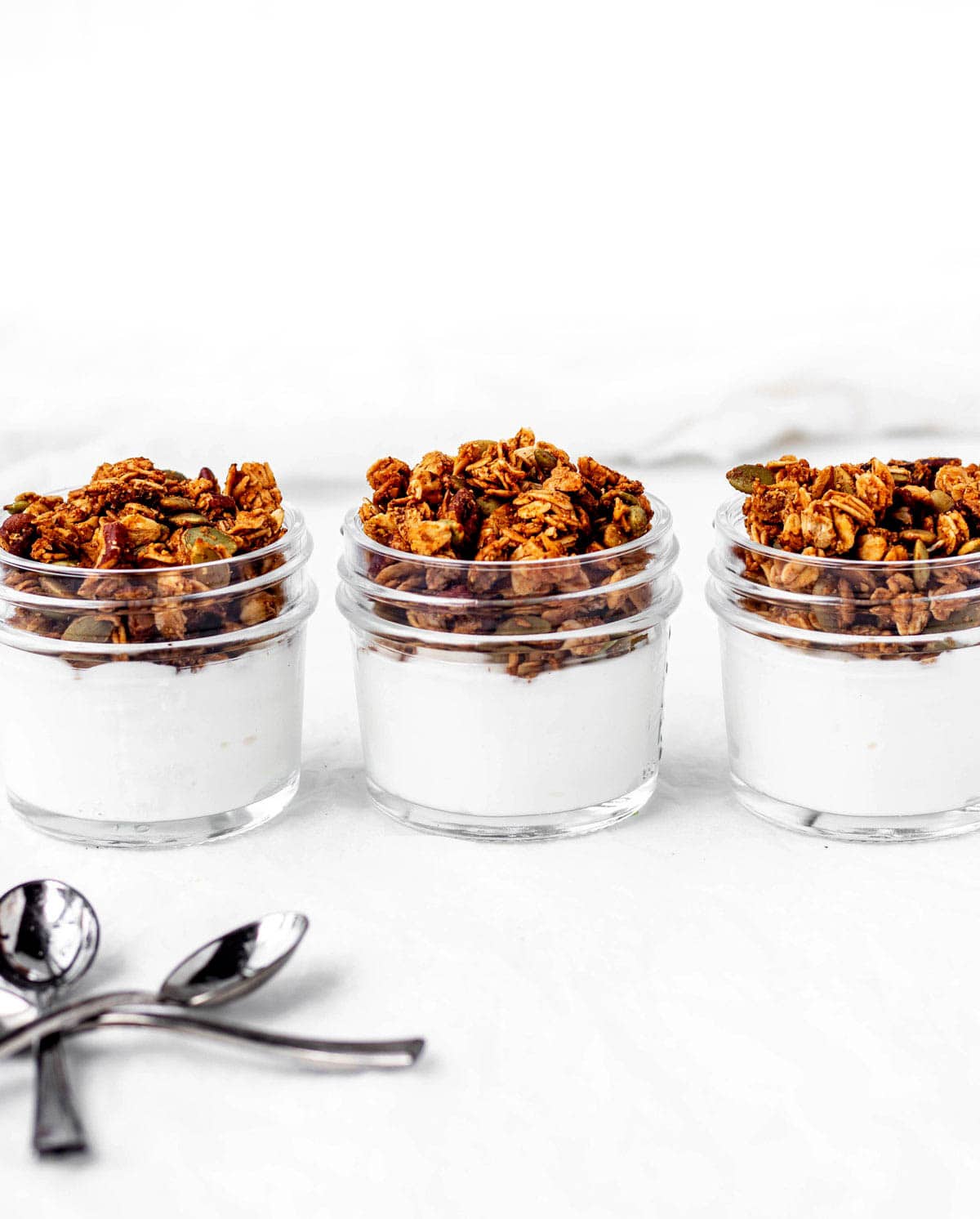 Three jars of yogurt topped with pumpkin granola.