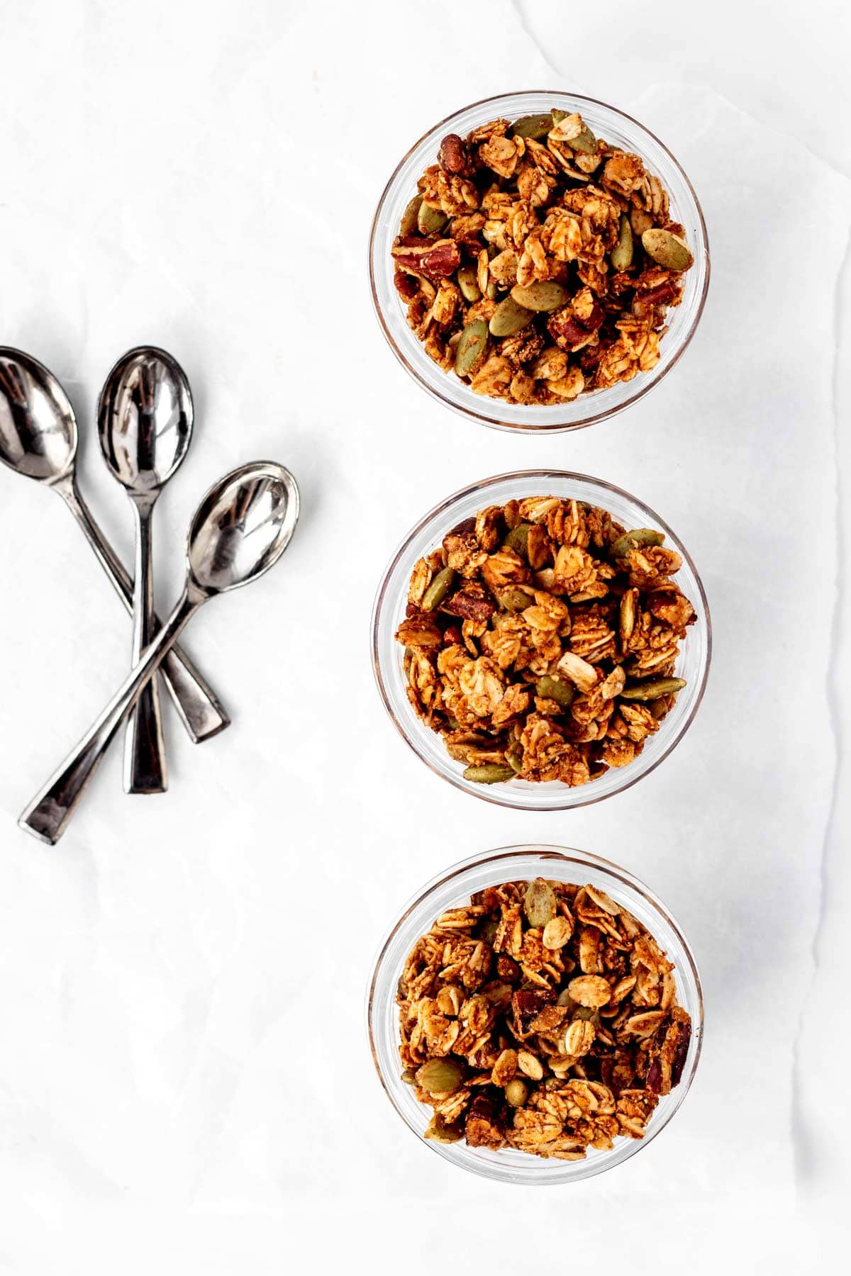 Three jars of pumpkin seed and flax granola served over yogurt with three spoons.