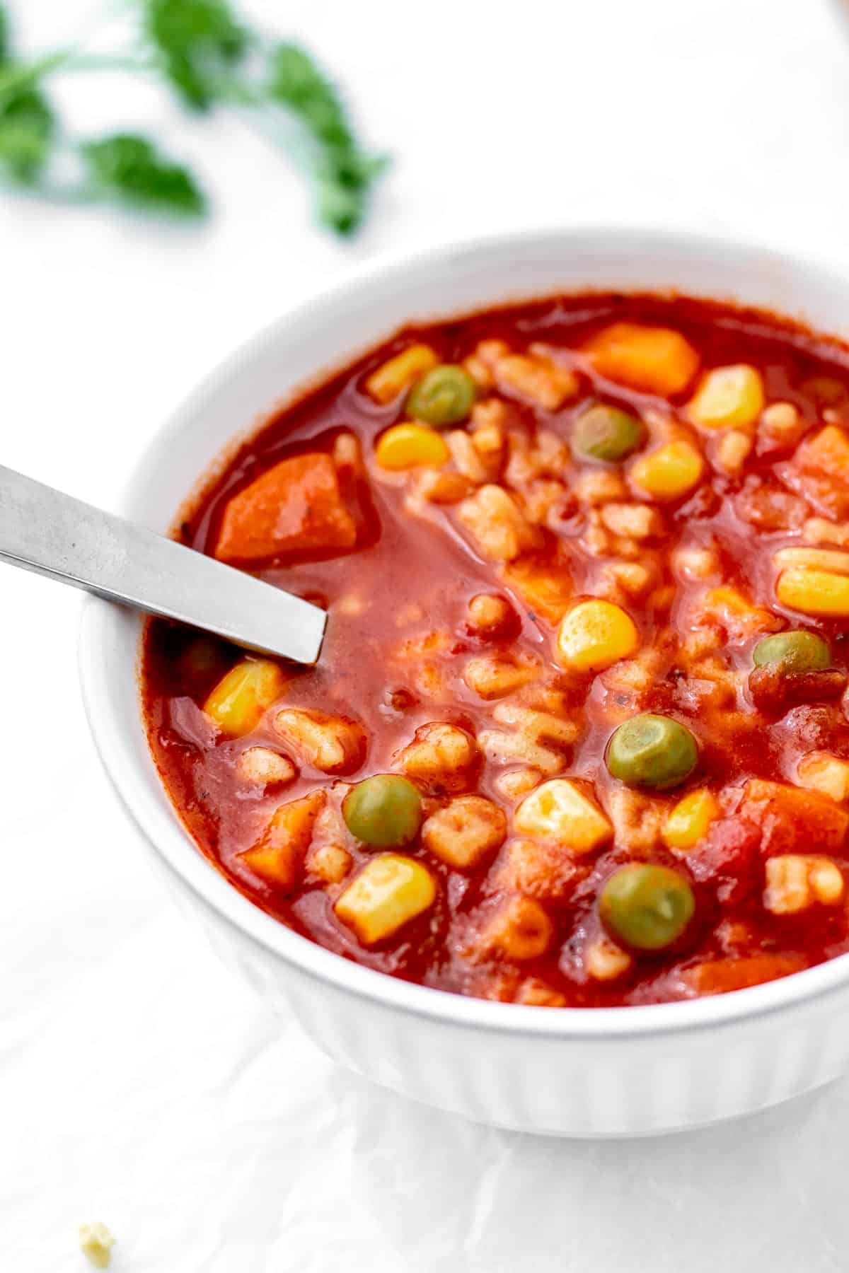 A close up image of veggie noodle soup in a small white bowl with a spoon.