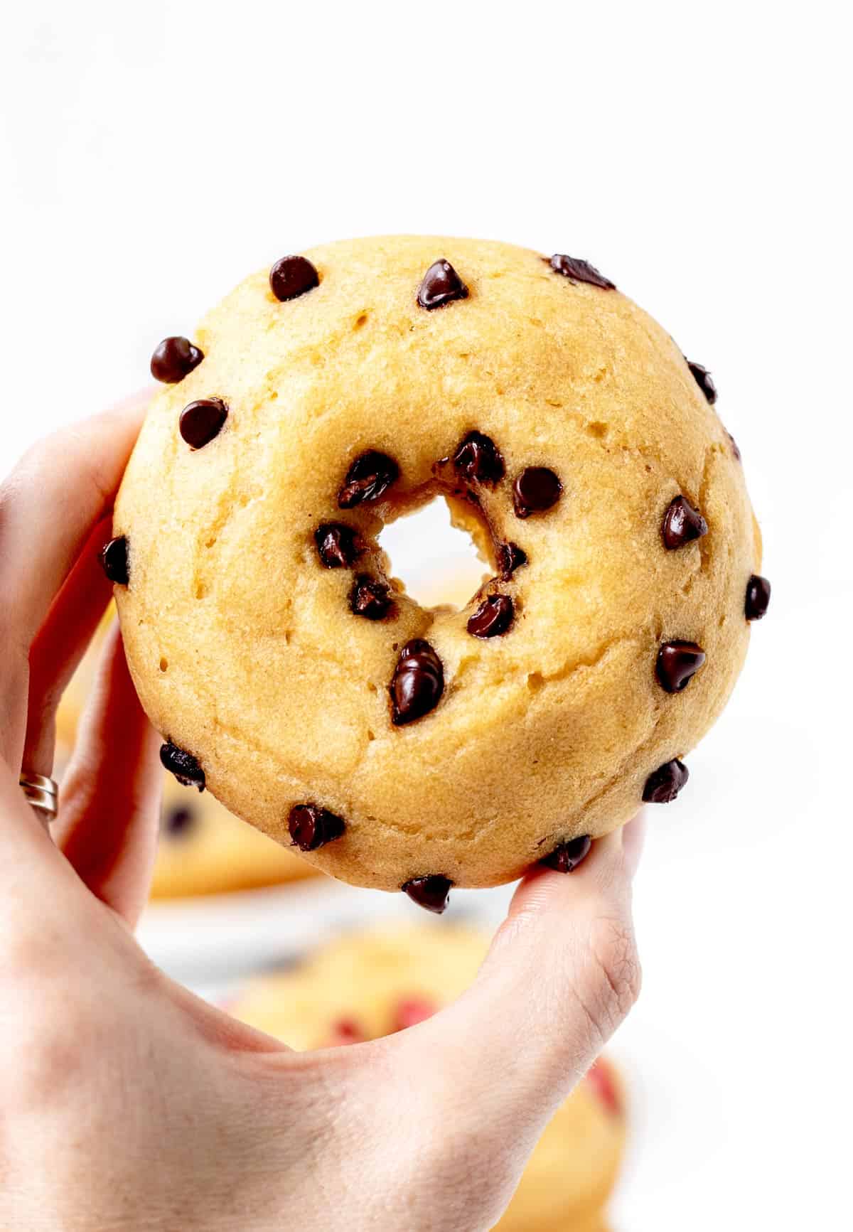 A hand holding up a pancake donut with chocolate chips.