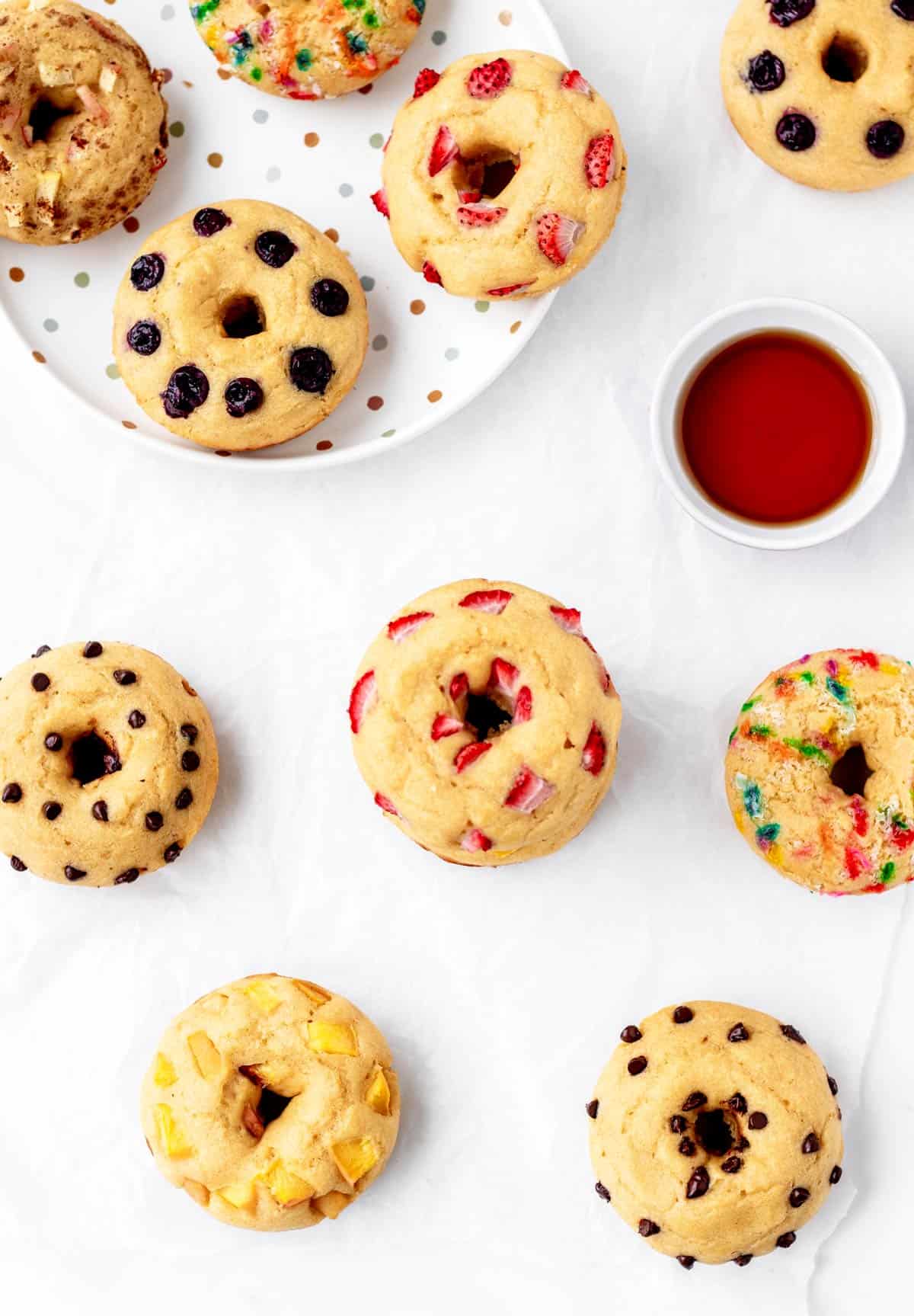 Pancake batter donuts on a white background with different toppings.