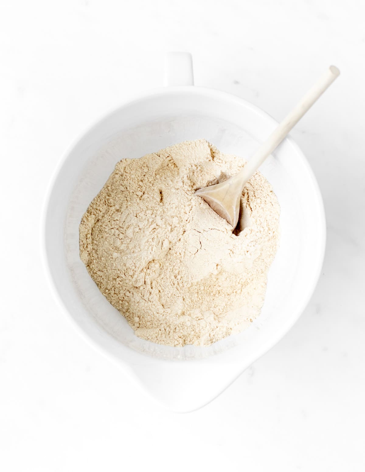 Dry ingredients mixed together in a white bowl with a wooden spoon.