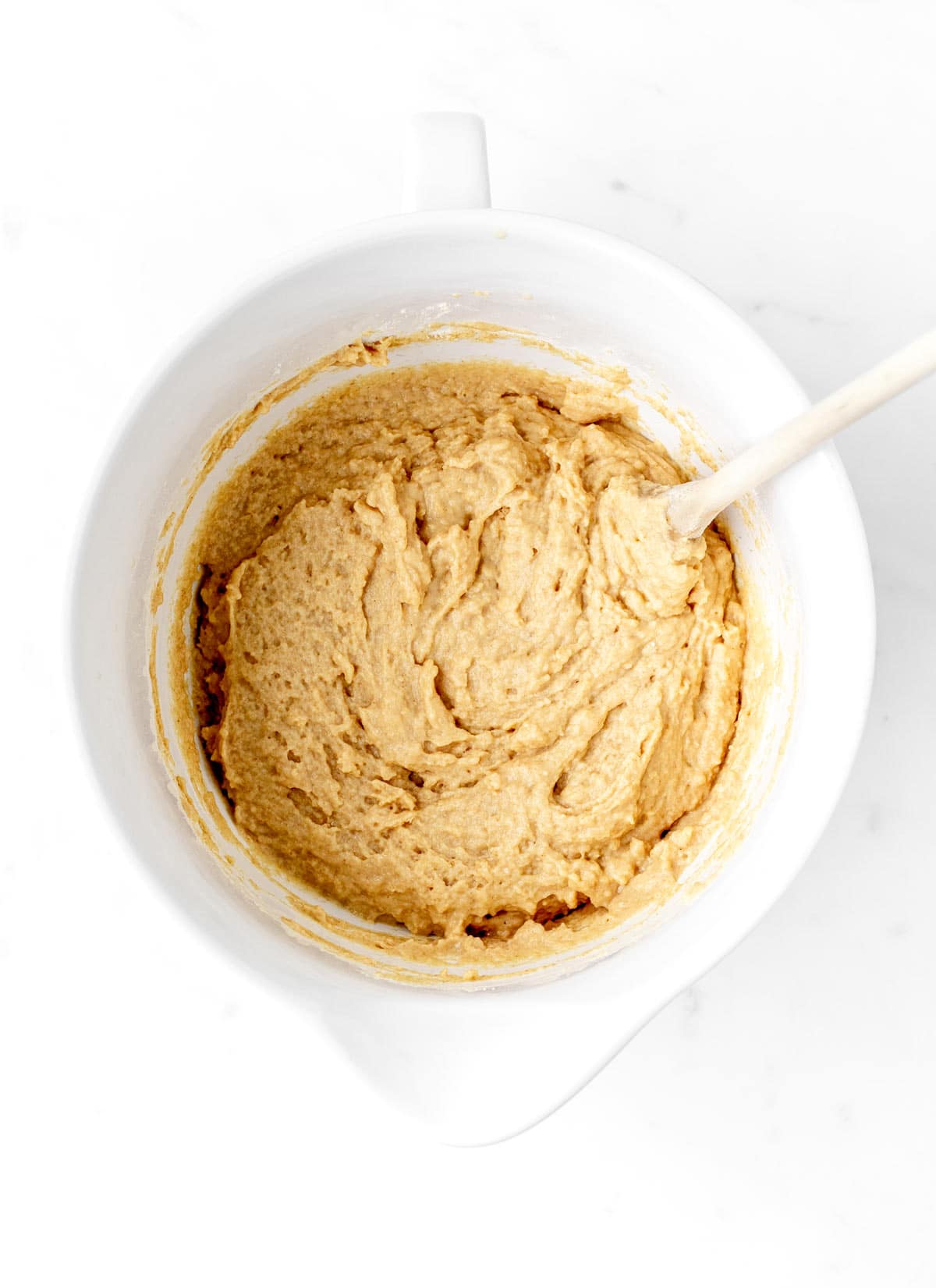 Wet and dry ingredients combined in a white bowl with a wooden spoon.