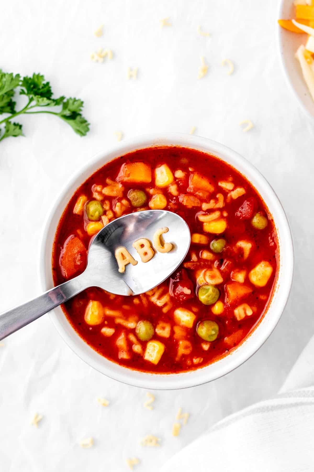 A bowl of tomato alphabet soup with "ABC" letters on a spoon.