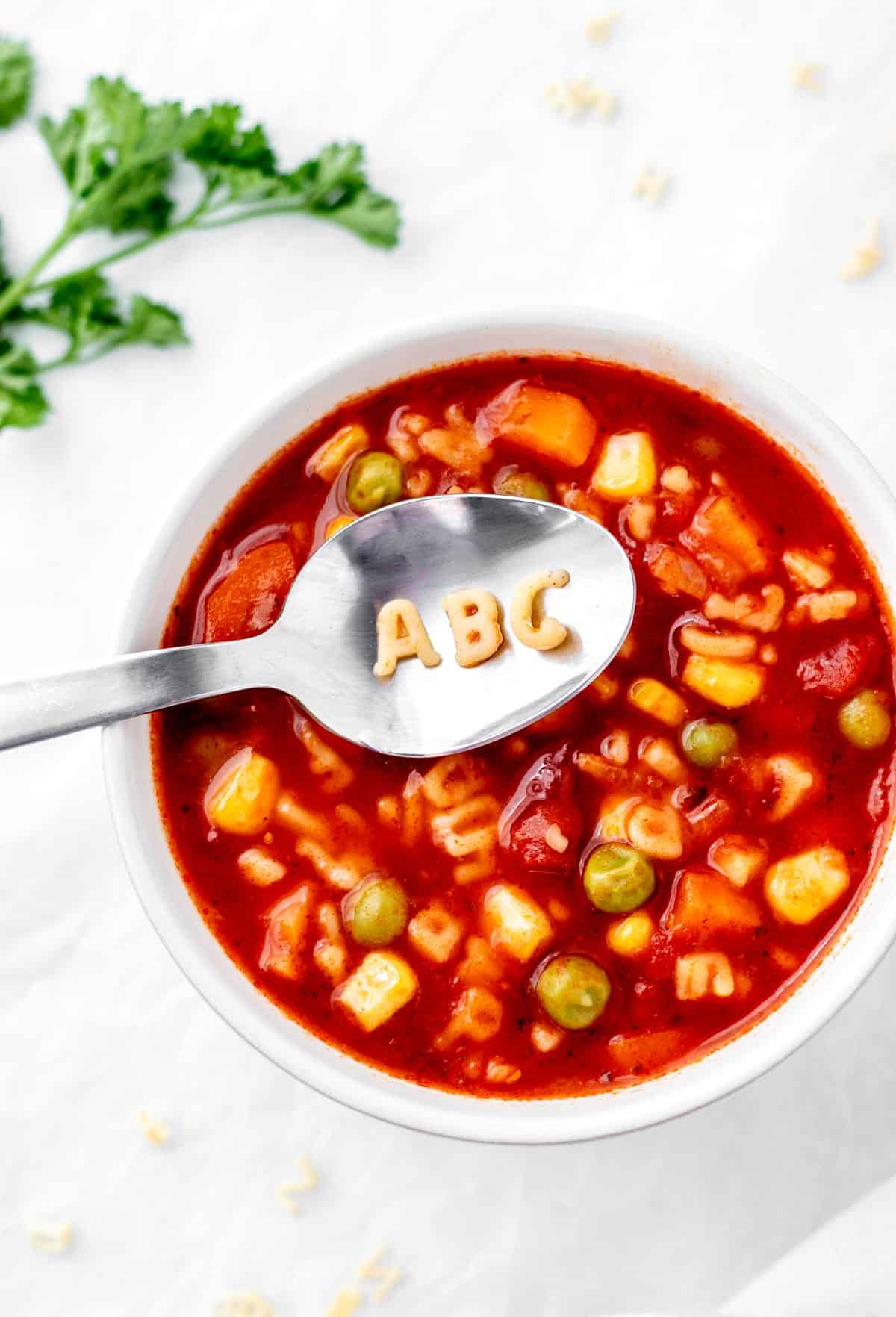 Vegetable noodle soup in a bowl with a spoon with "ABC" written on it with noodles.