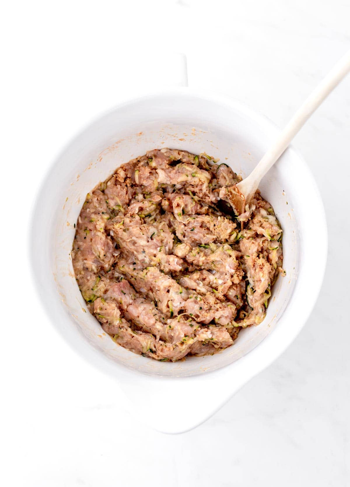 Turkey burger slider mixture in a large white bowl with a wooden spoon.