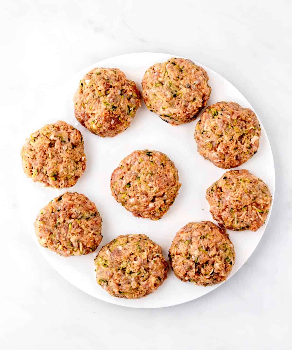 Ground turkey slider patties on a white plate ready to be cooked.