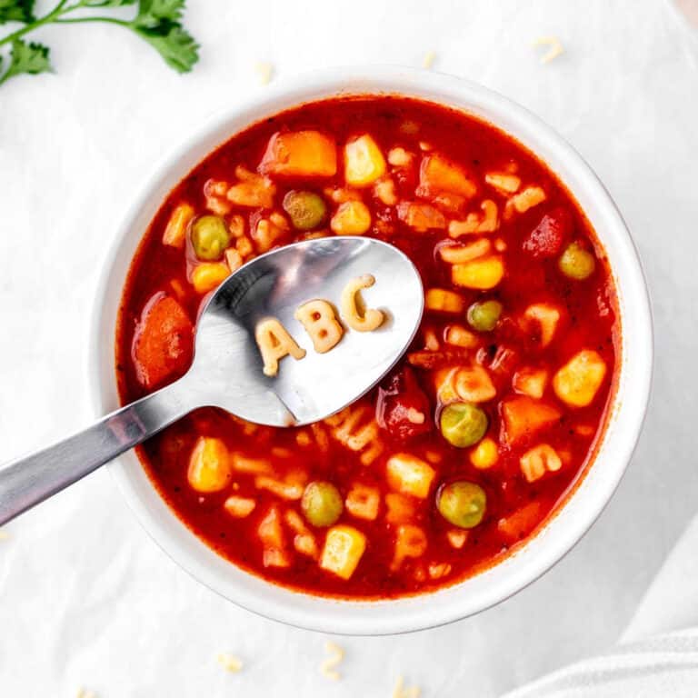 "ABC" noodles on a spoon over a bowl of veggie noodle soup.