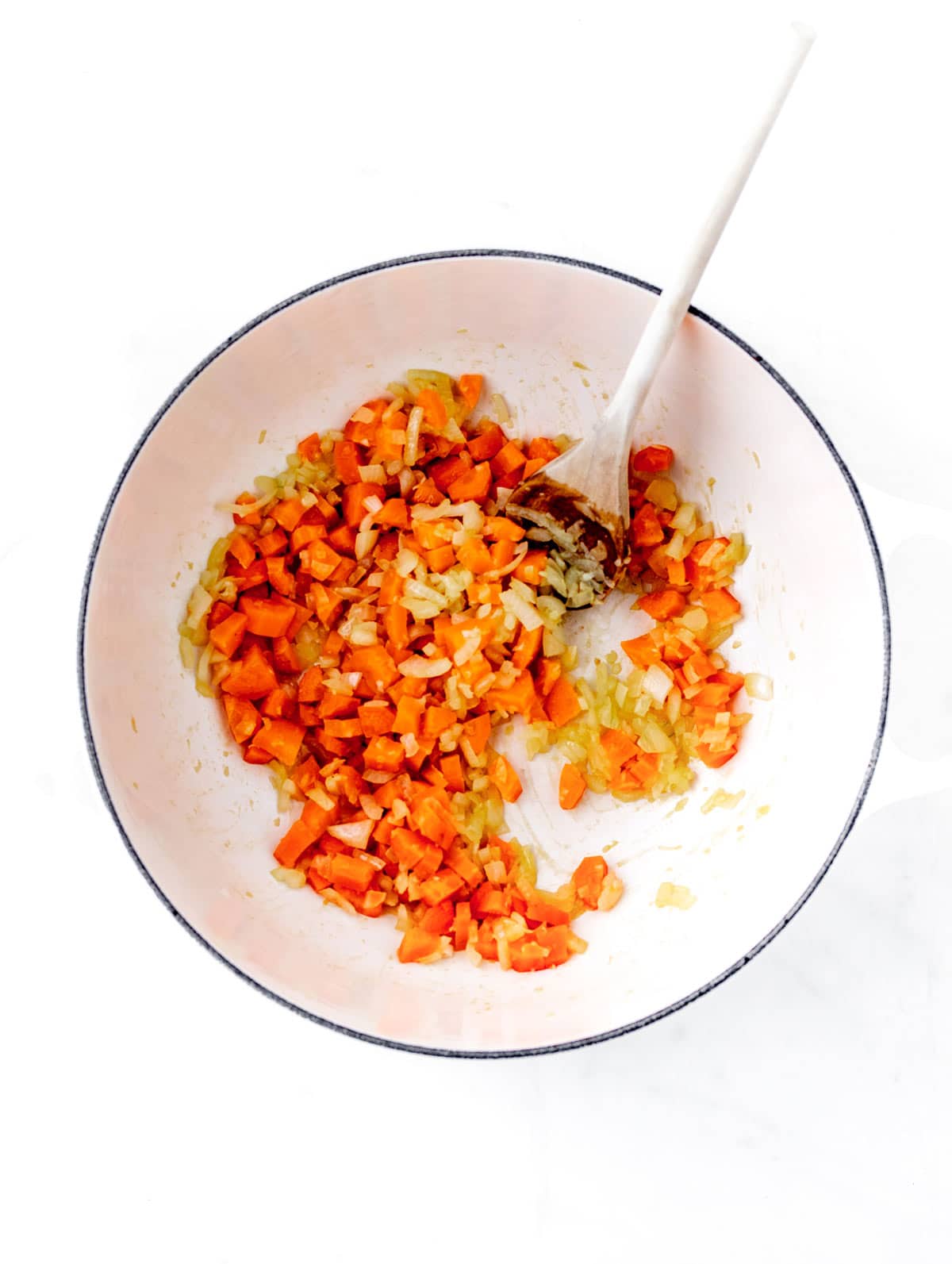 Carrots, onion and garlic being sauteed in a pot with a wooden spoon.