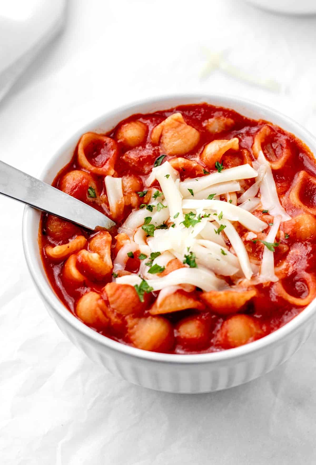 A white bowl full of noodles, red sauce and cheese on top with a spoon.