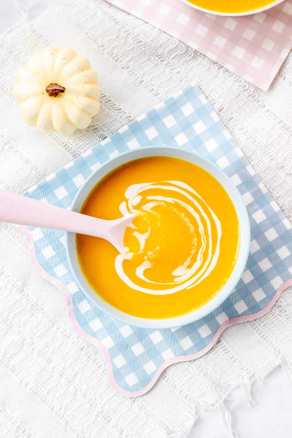 A blue bowl of pumpkin soup for babies next to a pumpkin.