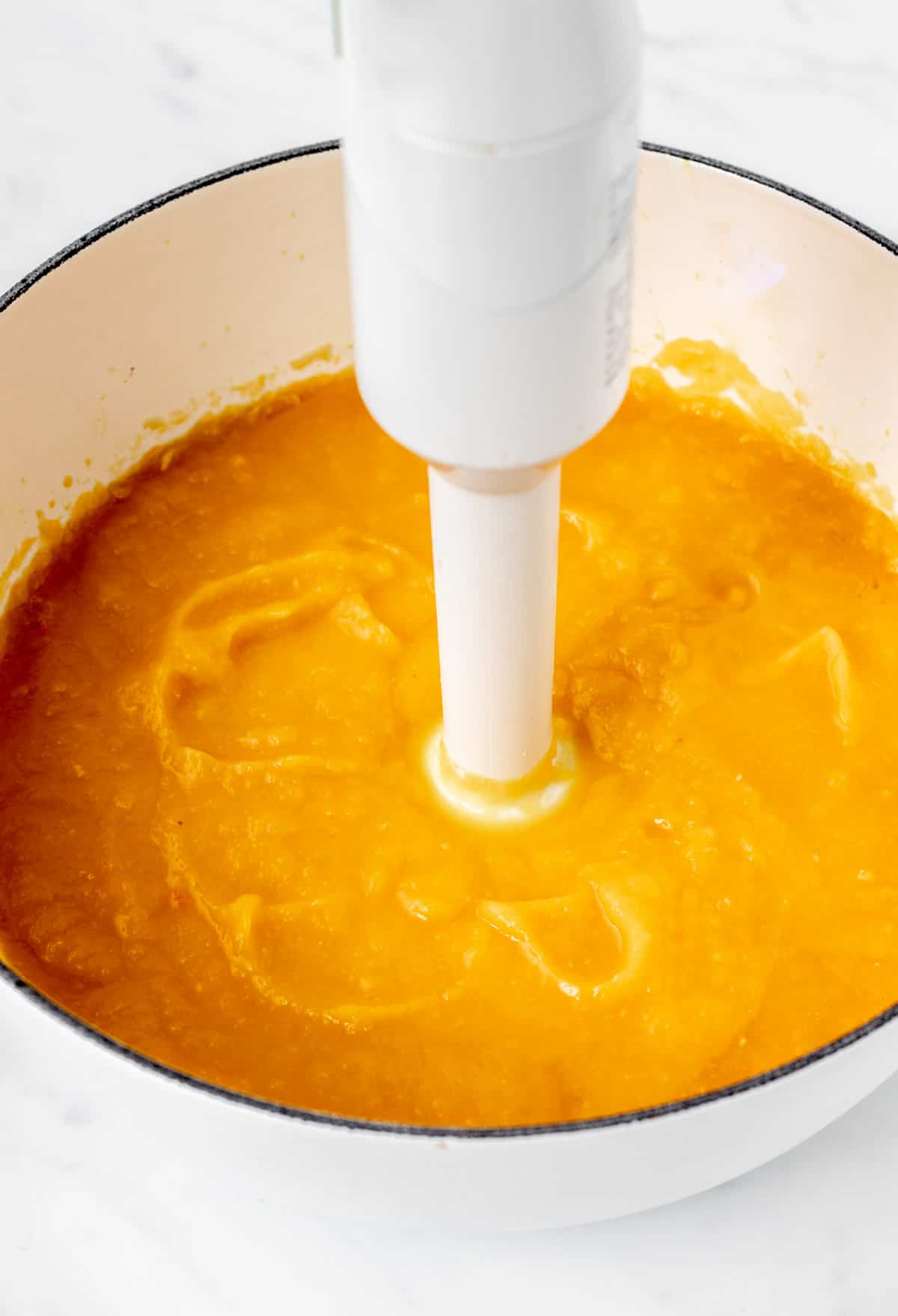 An immersion blender blending up pumpkin soup in a large pot.