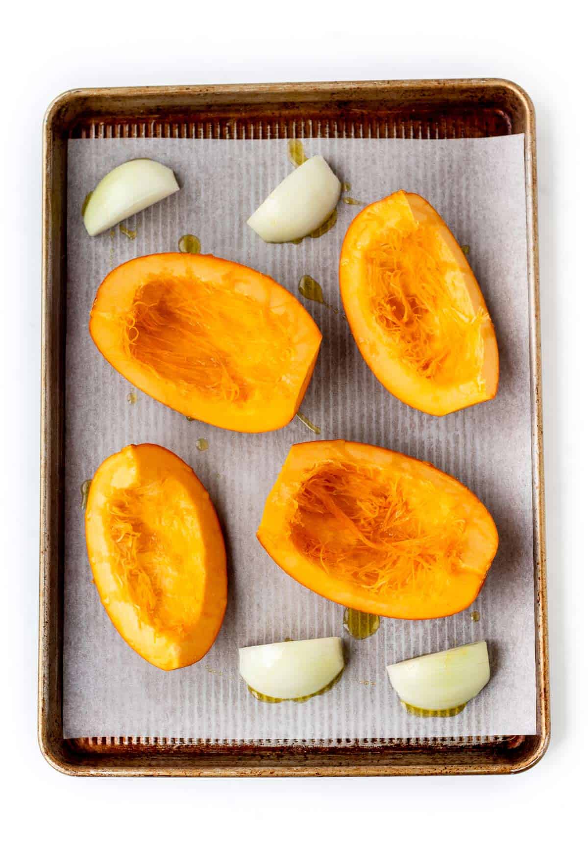 Pumpkin quarters being roasted on a baking sheet with onion.