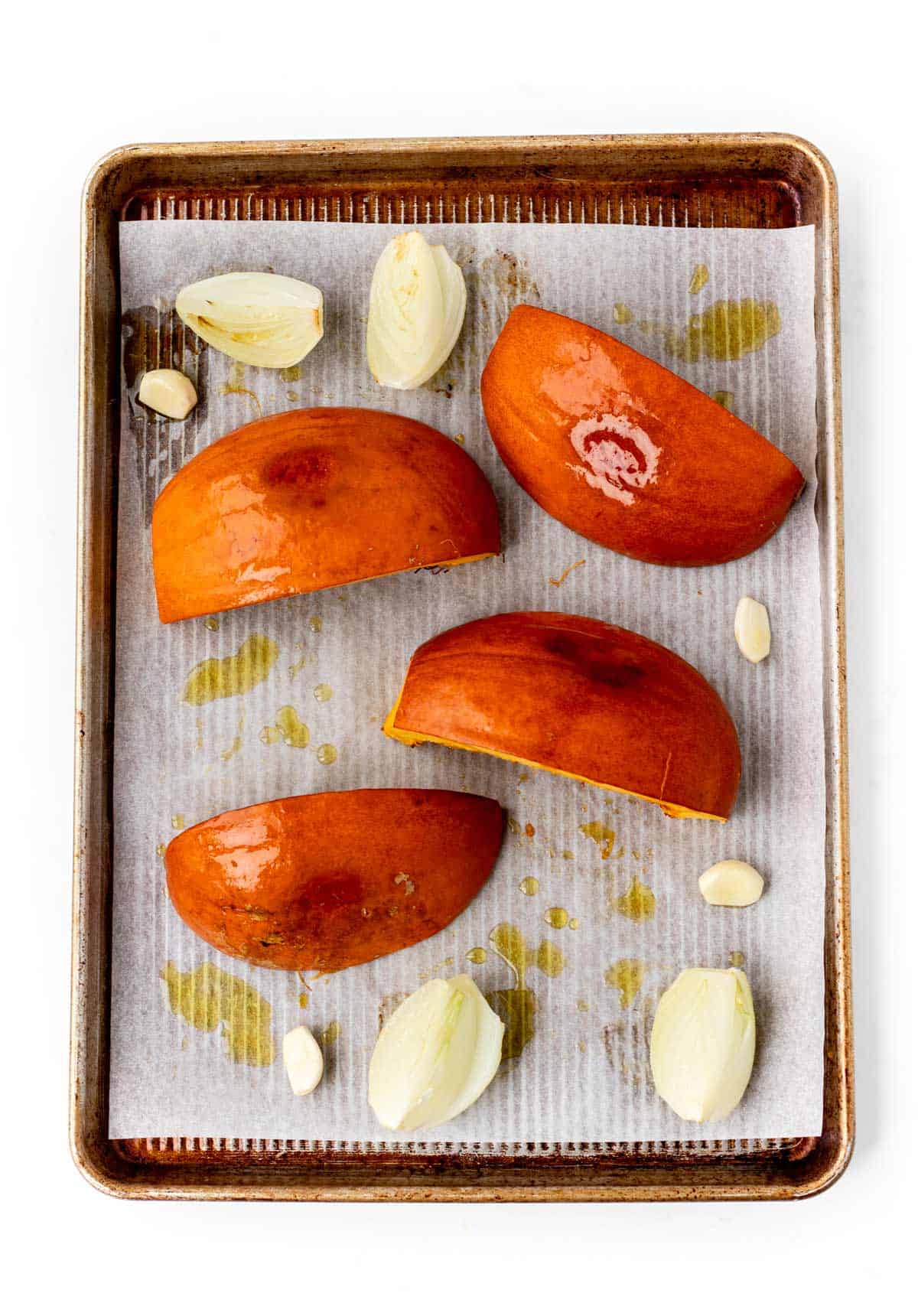 Roasted pumpkins, onions and garlic on a baking sheet.