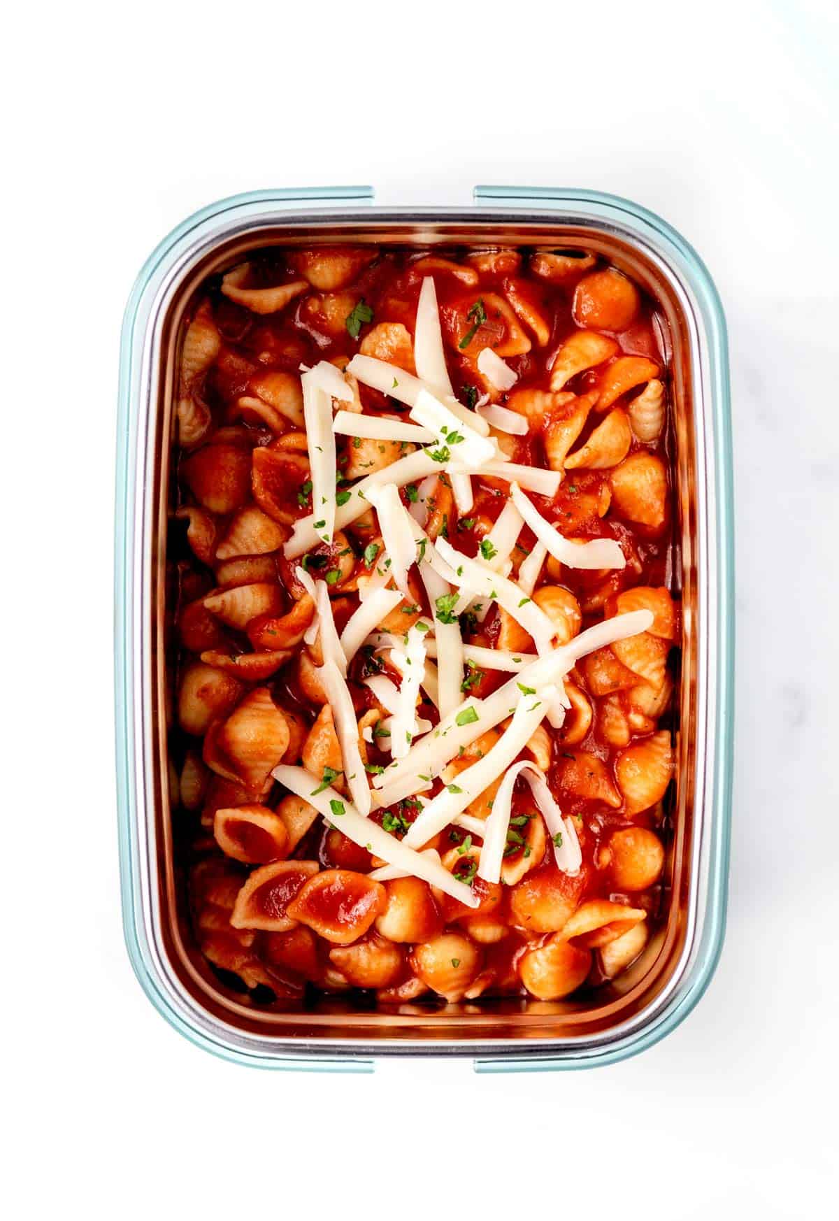 A glass container full of noodles, red sauce and cheese on top.