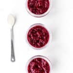 Three jars filled with berry chia jam with a spoon next to them.