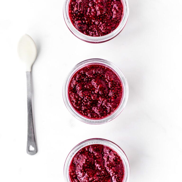 Three jars filled with berry chia jam with a spoon next to them.