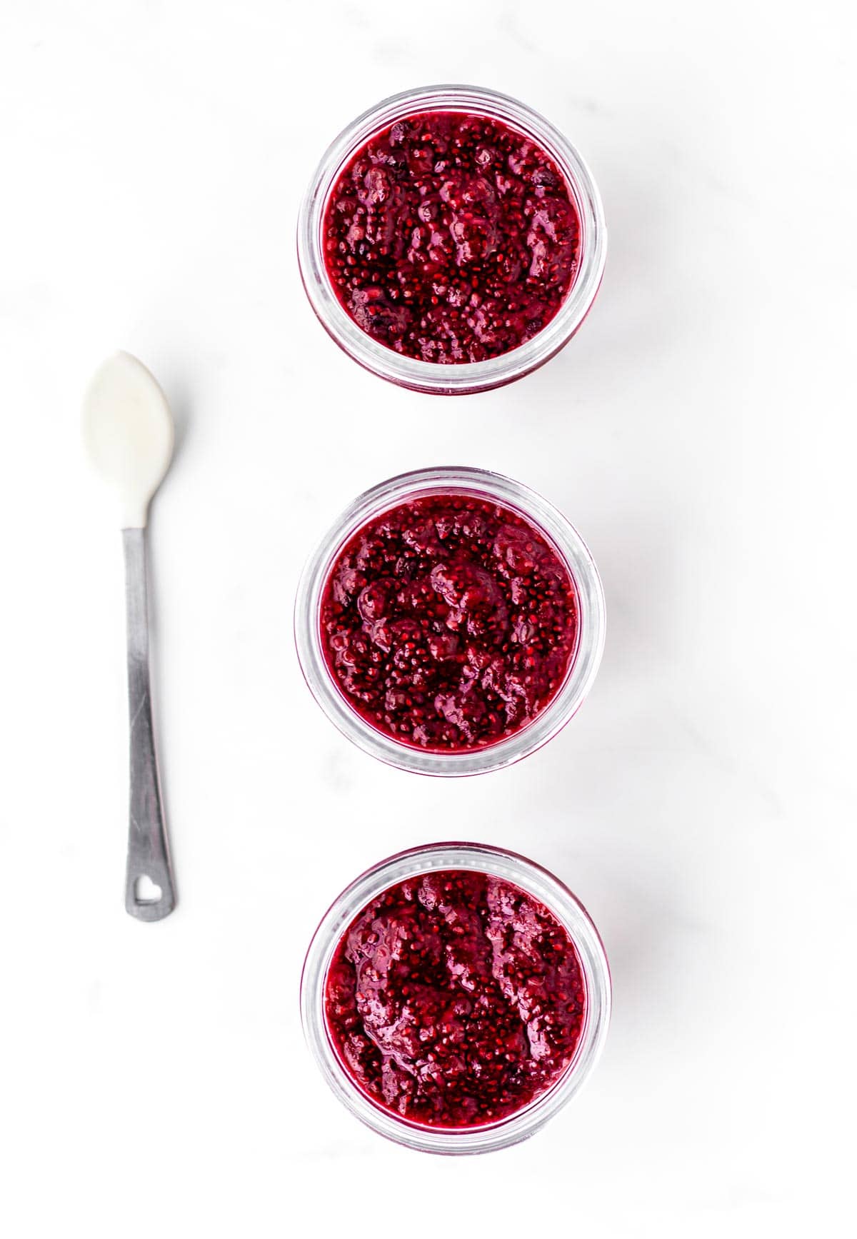 An overhead image of three small jars filled with baby jam and a spoon.