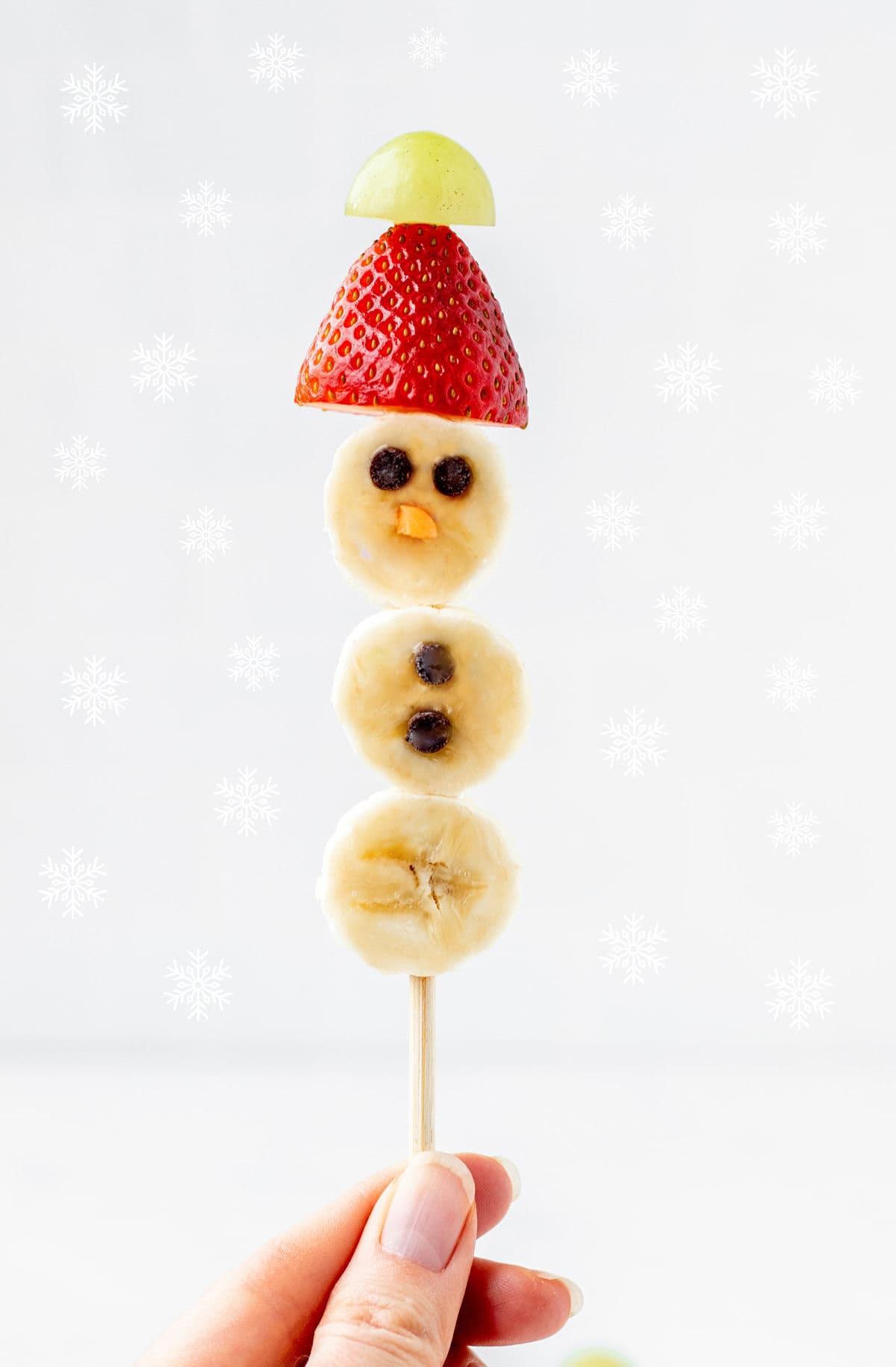 A banana snowman on a stick with snowflakes in the background.