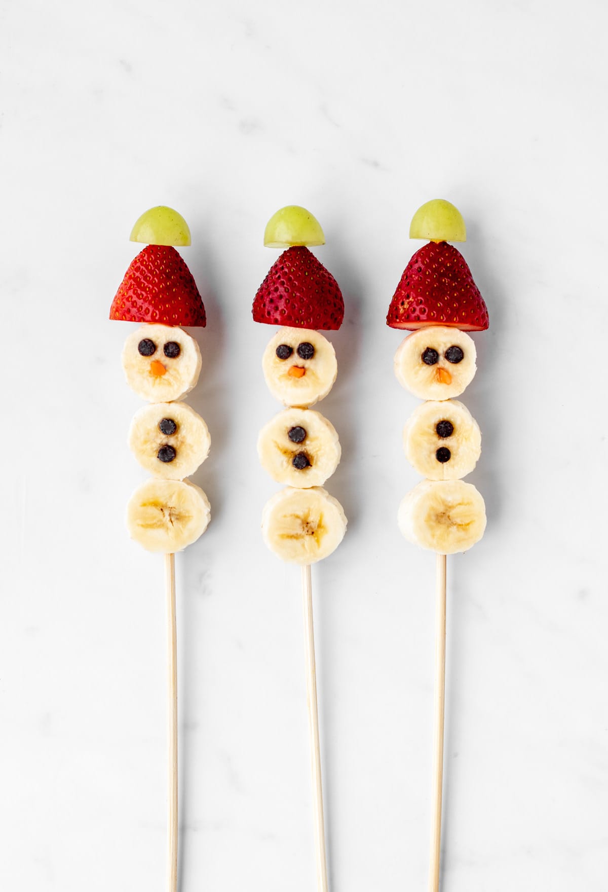 Three banana snowmen on sticks with strawberry hats.