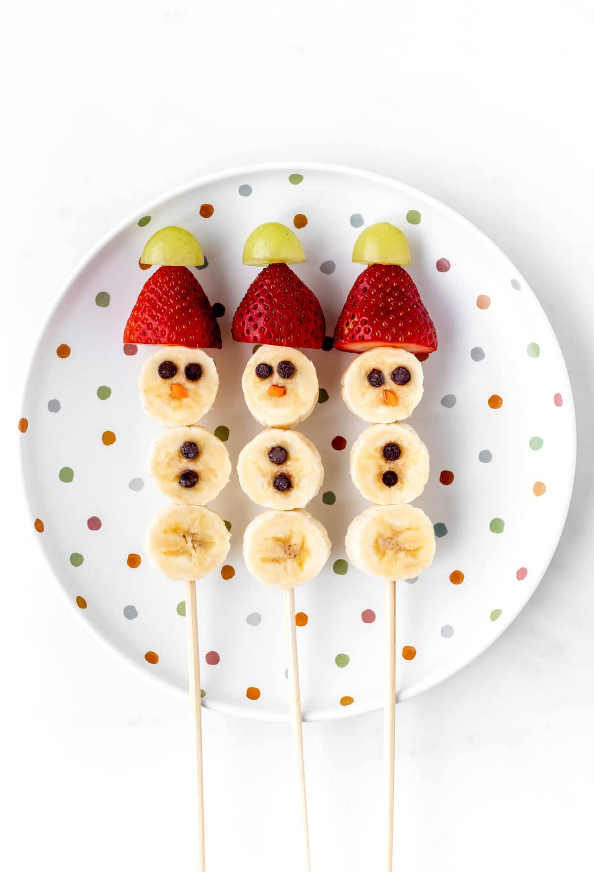 A polka dot plate with three banana snowmen on sticks.