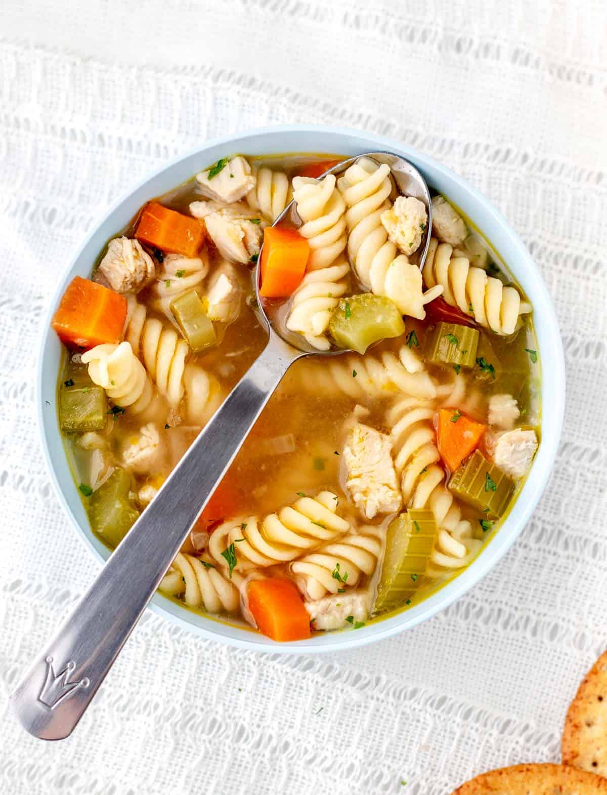 Chicken noodle soup for babies in a blue bowl with a spoon.