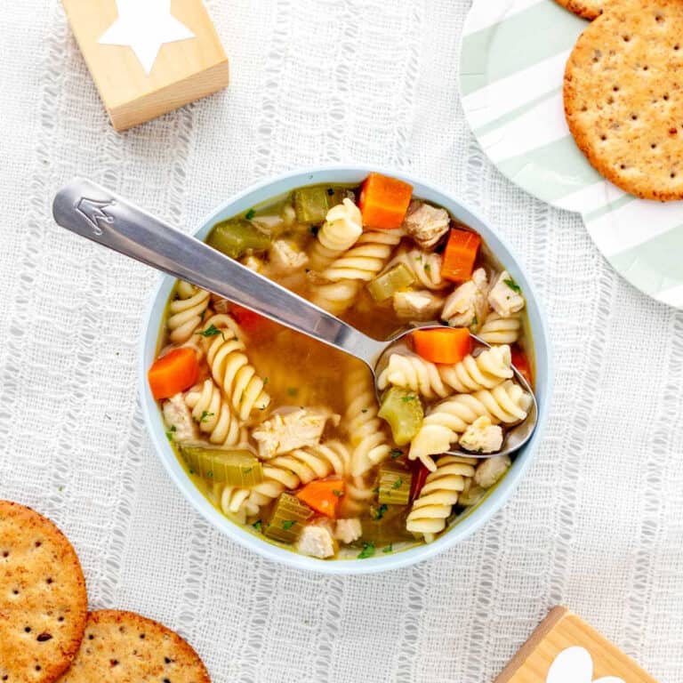 A bowl of baby chicken noodle soup with a spoon.