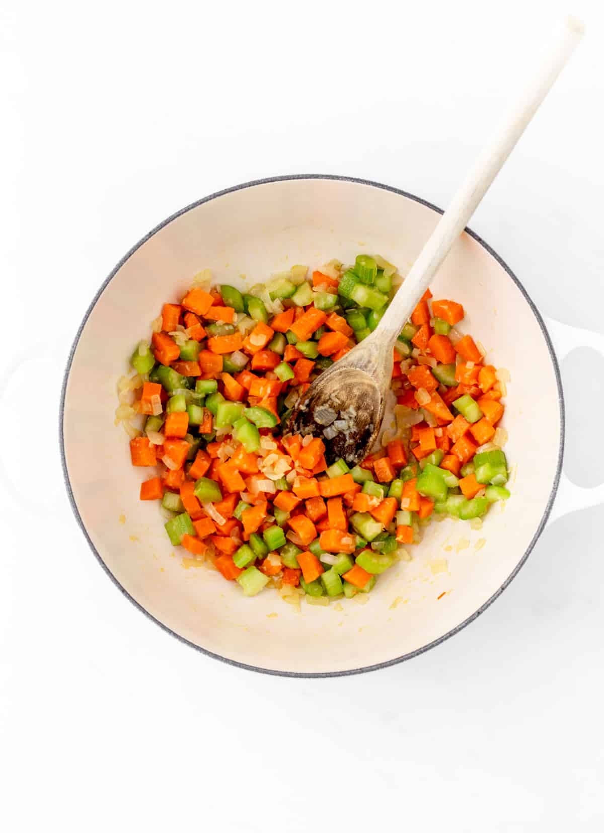 Chopped celery and carrots in a bowl with a wooden spoon.