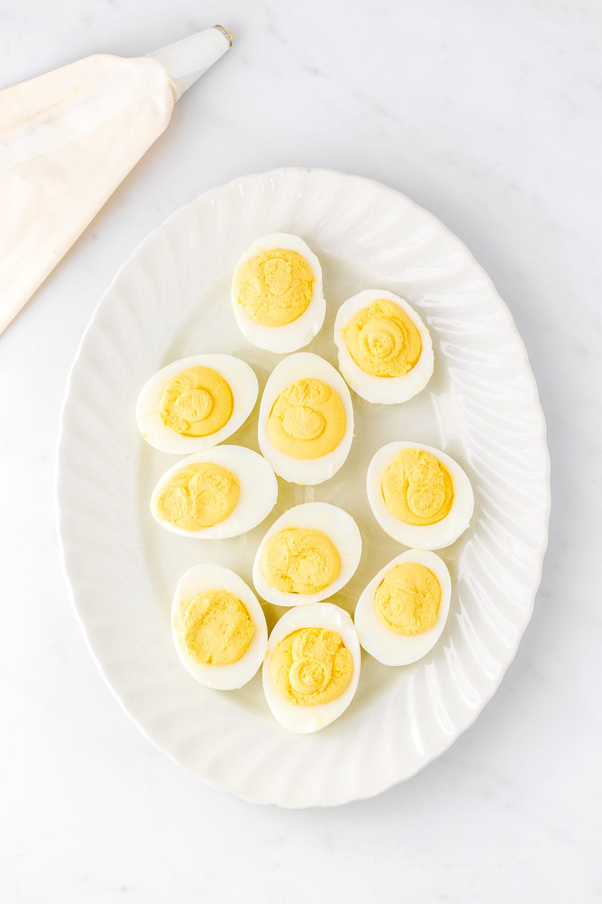 Greek yogurt deviled eggs on a tray with a piping bag.