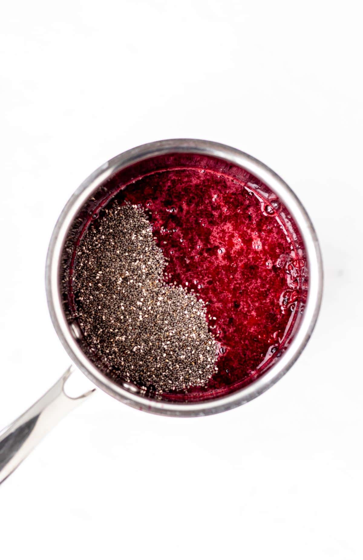 Chia seeds added to mashed berries in a small pot to make jam.