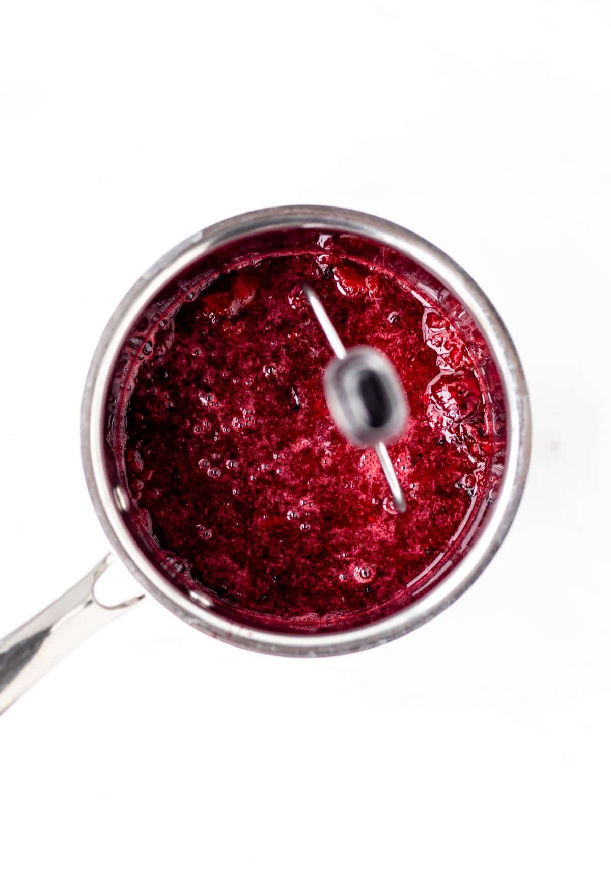 A potato masher mashing cooked berries in a small pot.