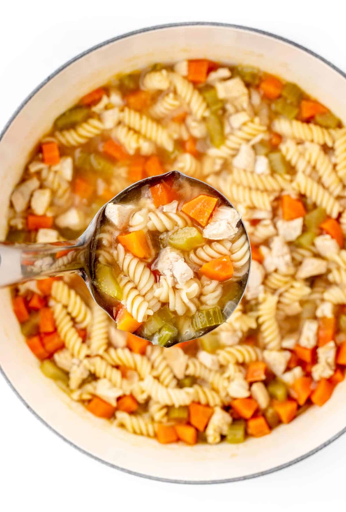 Chicken noodle soup for babies in a white bowl with a ladle taking out a scoop.