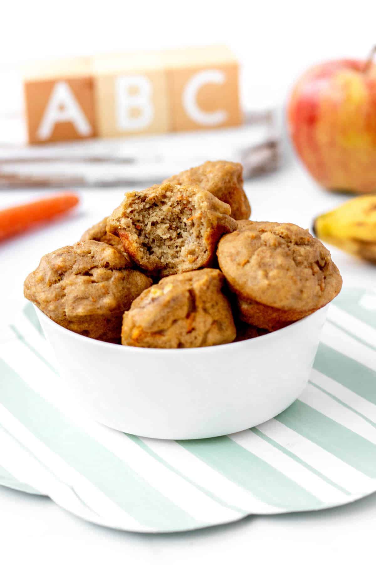 Abc muffins in a white bowl with bite taken out of top one.